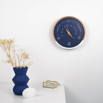 wooden barometer with navy blue dial on a wall next to a flower pot
