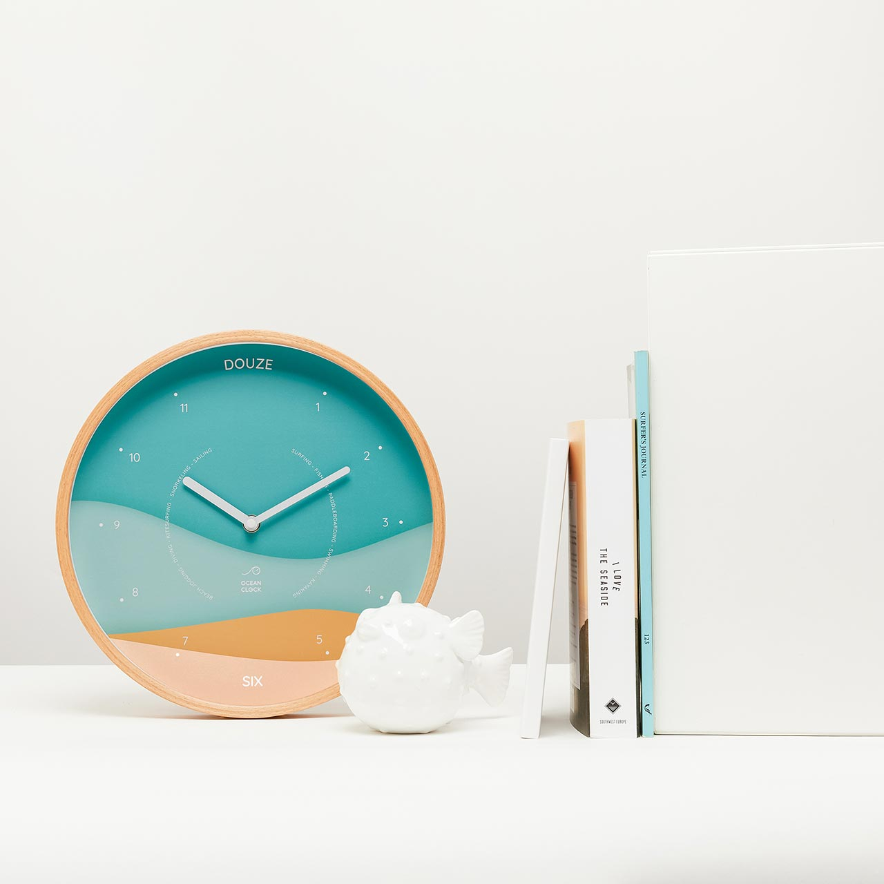 beige and turquoise clock in french next to books and white fish